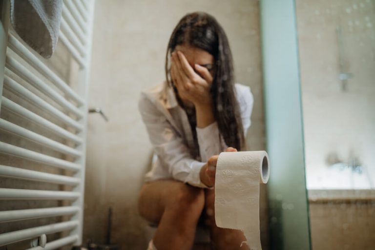 Frau sitzt mit Klopapier Rolle in der Hand auf der Toilette wegen Verstopfung